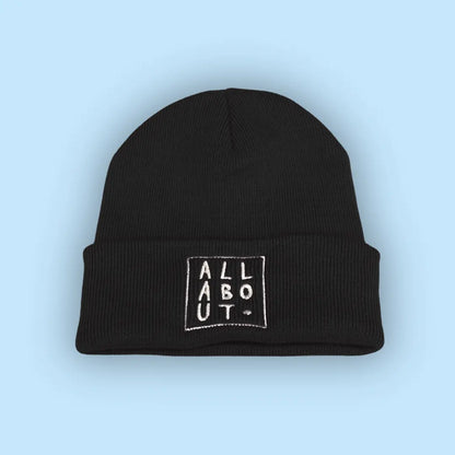 A black knit beanie hat with a folded cuff, featuring
 a white embroidered square logo on the front that 
reads 'ALL ABOUT.' in vertical letters, set against a 
solid light blue background.